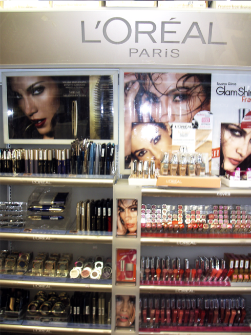 Esposizione di prodotti per il trucco L'Oréal Paris con prodotti sugli scaffali e poster promozionali raffiguranti donne truccate.