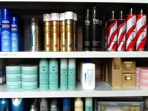 Scaffali pieni di vari prodotti per lo styling dei capelli in bombolette spray e barattoli.