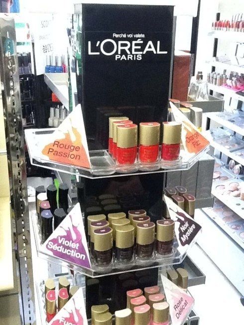 Espositore di smalti L'Oréal con flaconi rossi, viola e rosa. All'interno di un negozio.