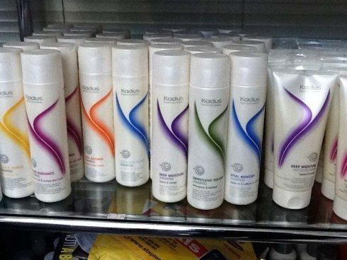 File di flaconi bianchi di prodotti per capelli con disegni curvi colorati su uno scaffale.