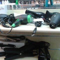Strumenti per lo styling dei capelli: asciugacapelli neri e verdi, piastre e fermagli su uno scaffale.
