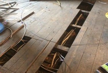 An exposed wooden floor with boards removed to reveal wiring and cables running through the joists An exposed wooden floor with boards removed to reveal wiring and cables running through the joists