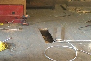A wood floor with a cutout section exposing wiring and tools scattered around A wood floor with a cutout section exposing wiring and tools scattered around