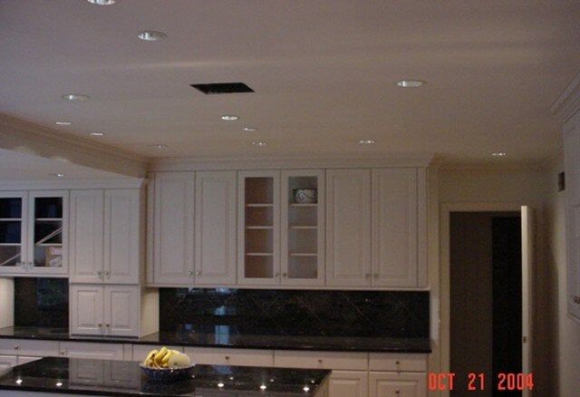Modern kitchen with white cabinets, black countertops, and a dark backsplash; doorway at right.
