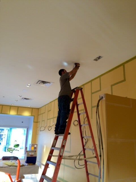 Worker on a ladder painting a ceiling in a room with yellow walls and green trim