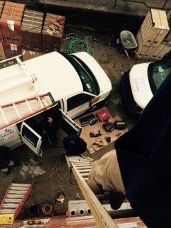Overhead view of white vans parked in a cluttered alley with boxes, tools, and cables scattered around