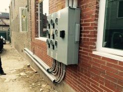 Gray electrical meter boxes mounted on a red brick wall outside a building