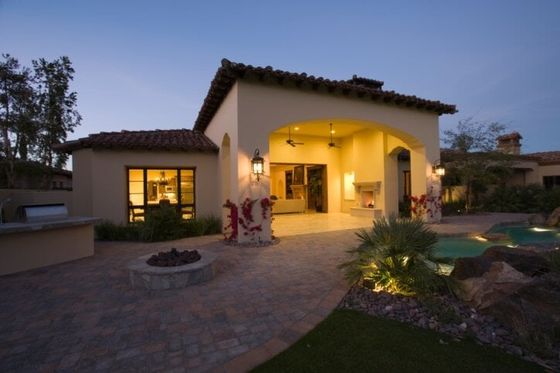 Modern stucco house at dusk with warm porch lights, stone patio, and landscaped yard