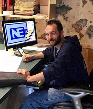 A man is working at a desk with a computer displaying an electrical company logo in an office area A man is working at a desk with a computer displaying an electrical company logo in an office area