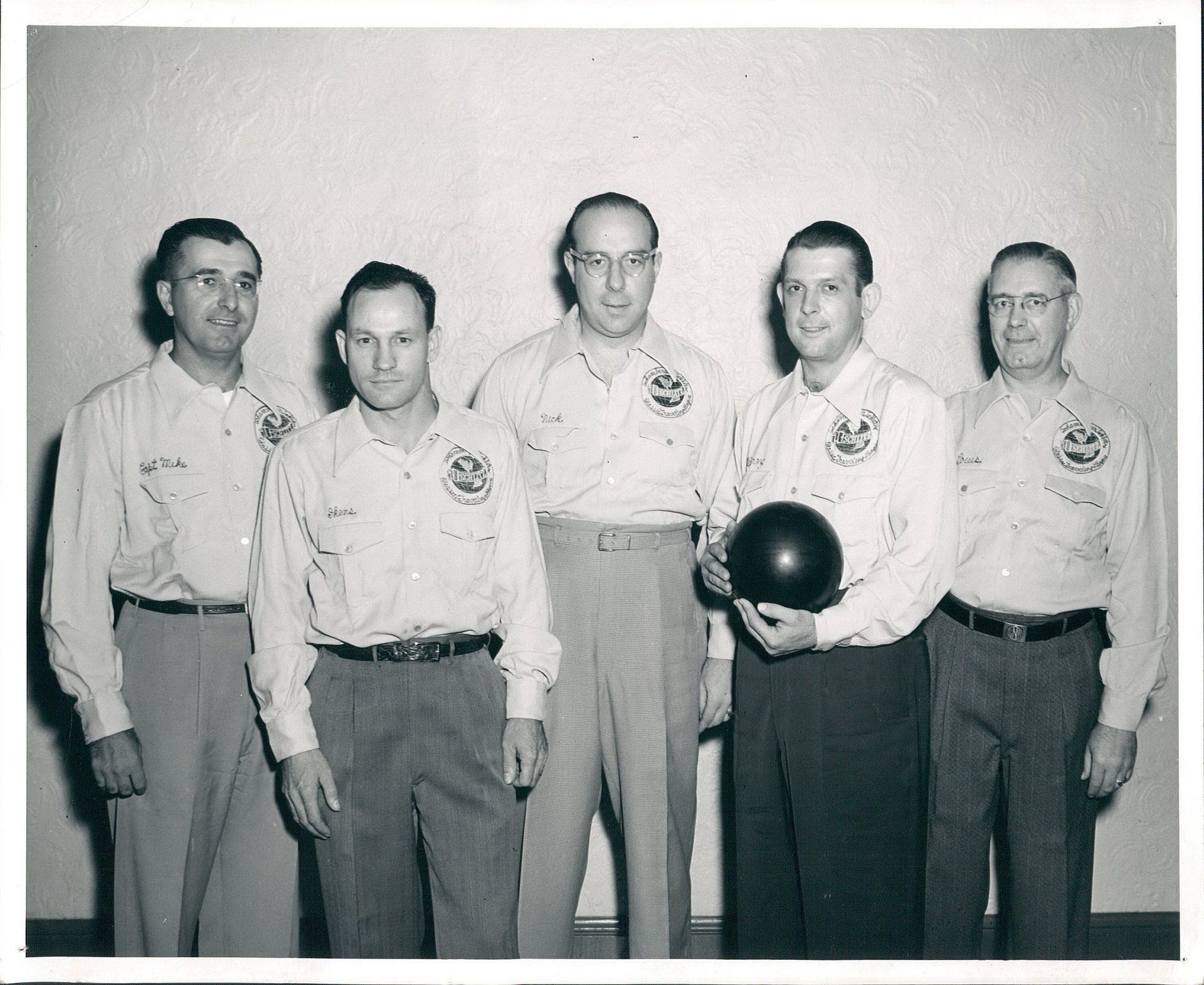 A group of men standing next to each other holding a bowling ball