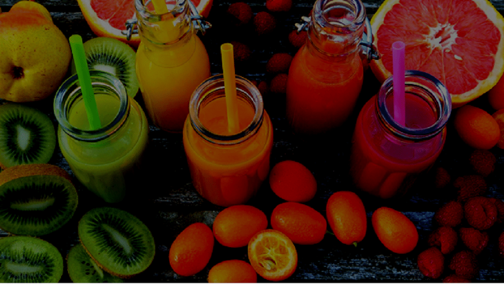Imagem colorida de frutas como Kiwi e tomates, sucos coloridos (verde, laranja, amarelo,vermelho) em potes de vidro e cadudos