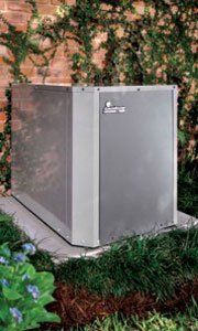 A large silver box is sitting in the grass next to a brick wall.