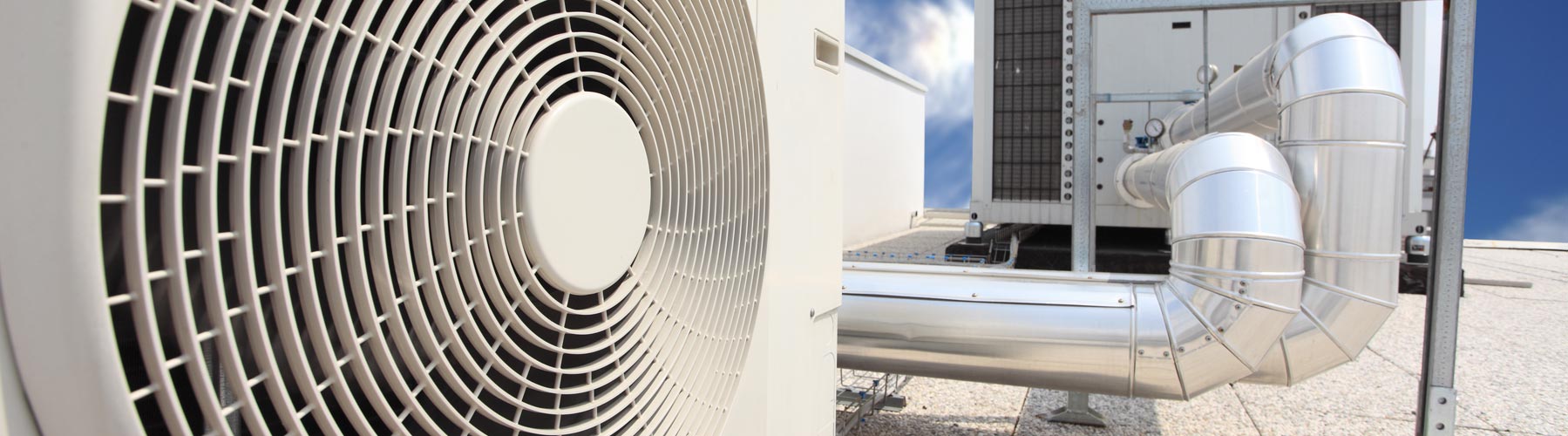 Air conditioning unit with fan grill and metal pipes against a blue sky.
