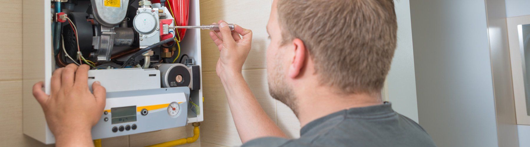 A man repairing a gas boiler with a screwdriver, indoors.