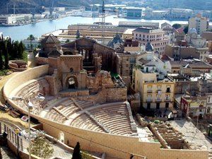 Ruins of an ancient Roman amphitheater in Málaga, Spain, with the city and harbor in the background.