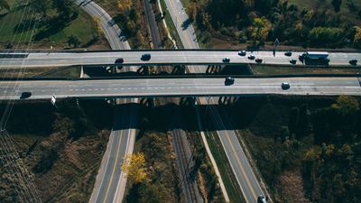 An aerial view of a highway overpass crossing over a road and railroad tracks, with vehicles driving on the bridge.