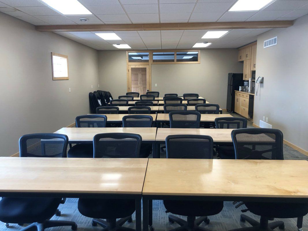 Rows of chairs and light-colored tables arranged in a conference room, facing a doorway at the back of the space.