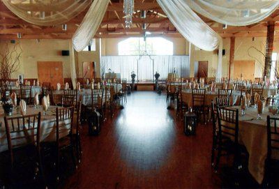 A banquet hall set for a reception with round tables, draped ceiling fabric, and a central aisle leading to a stage.