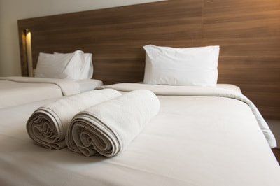 Two beds with white linens and folded towels in a room with a wood-paneled headboard.