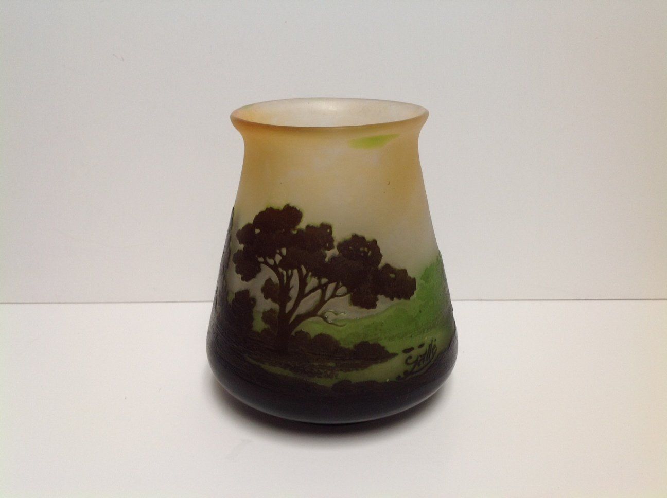A small vase with trees on it sits on a white surface