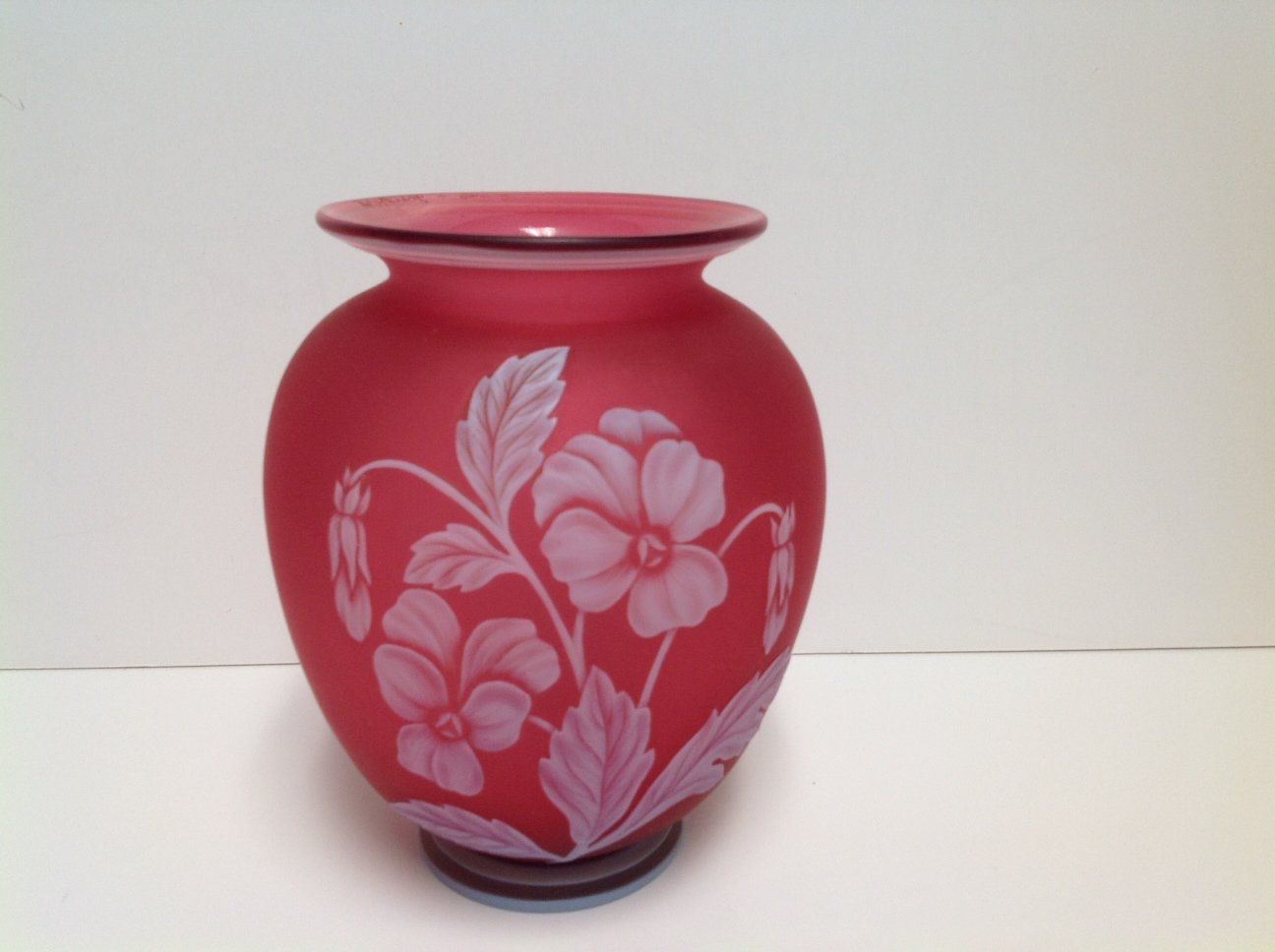 A red vase with purple flowers and leaves on it