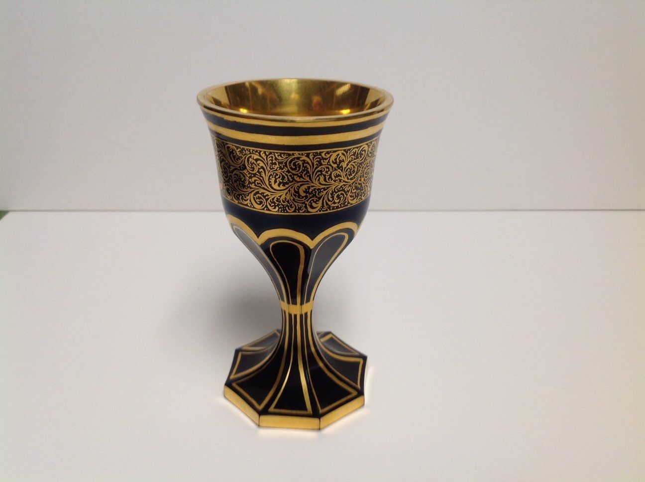 A black and gold goblet is sitting on a white surface