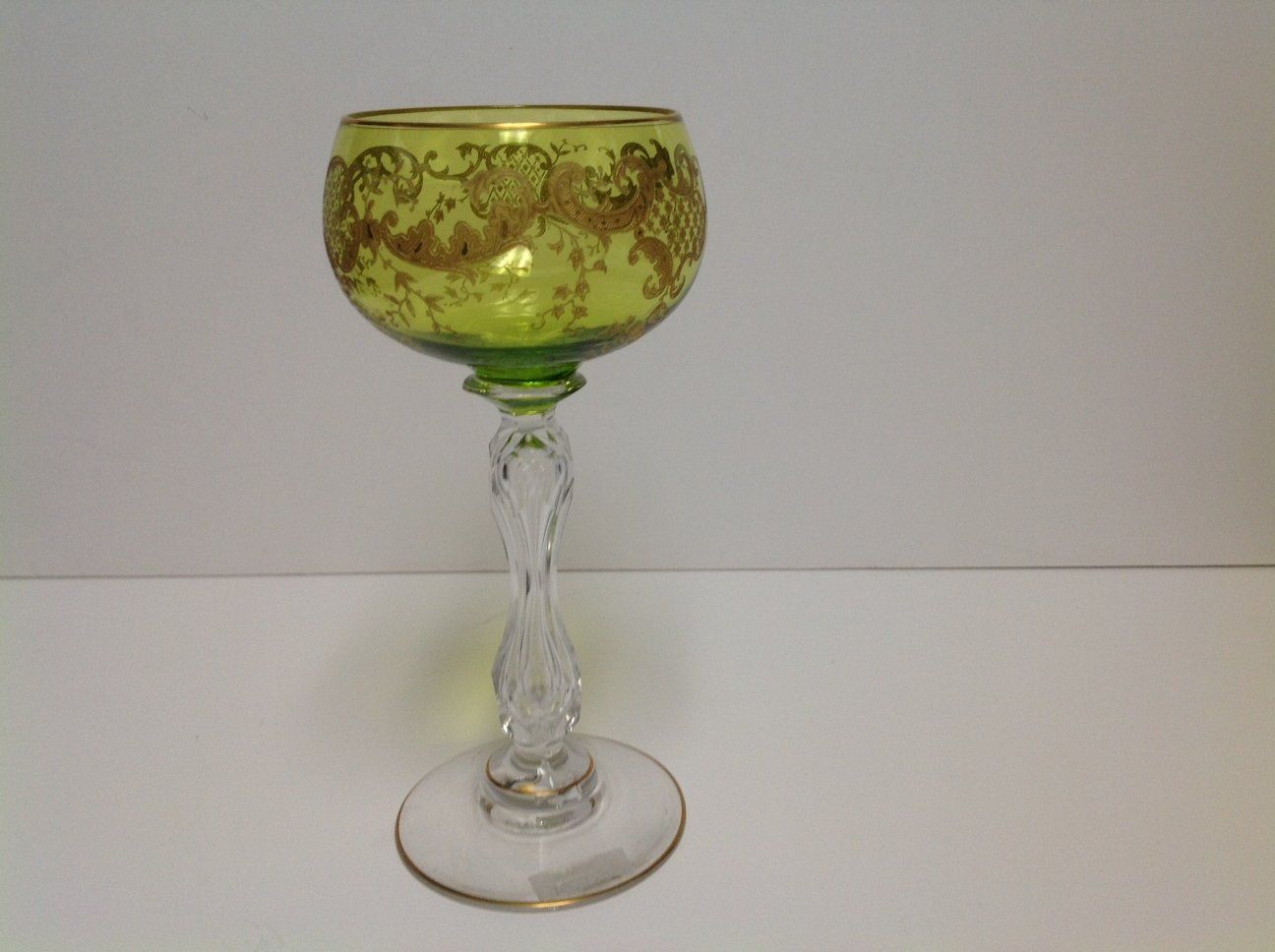 A green wine glass with a gold design on it