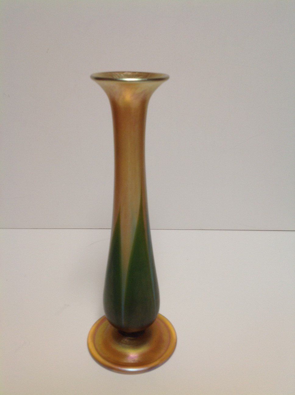 A green and gold vase is sitting on a white table.