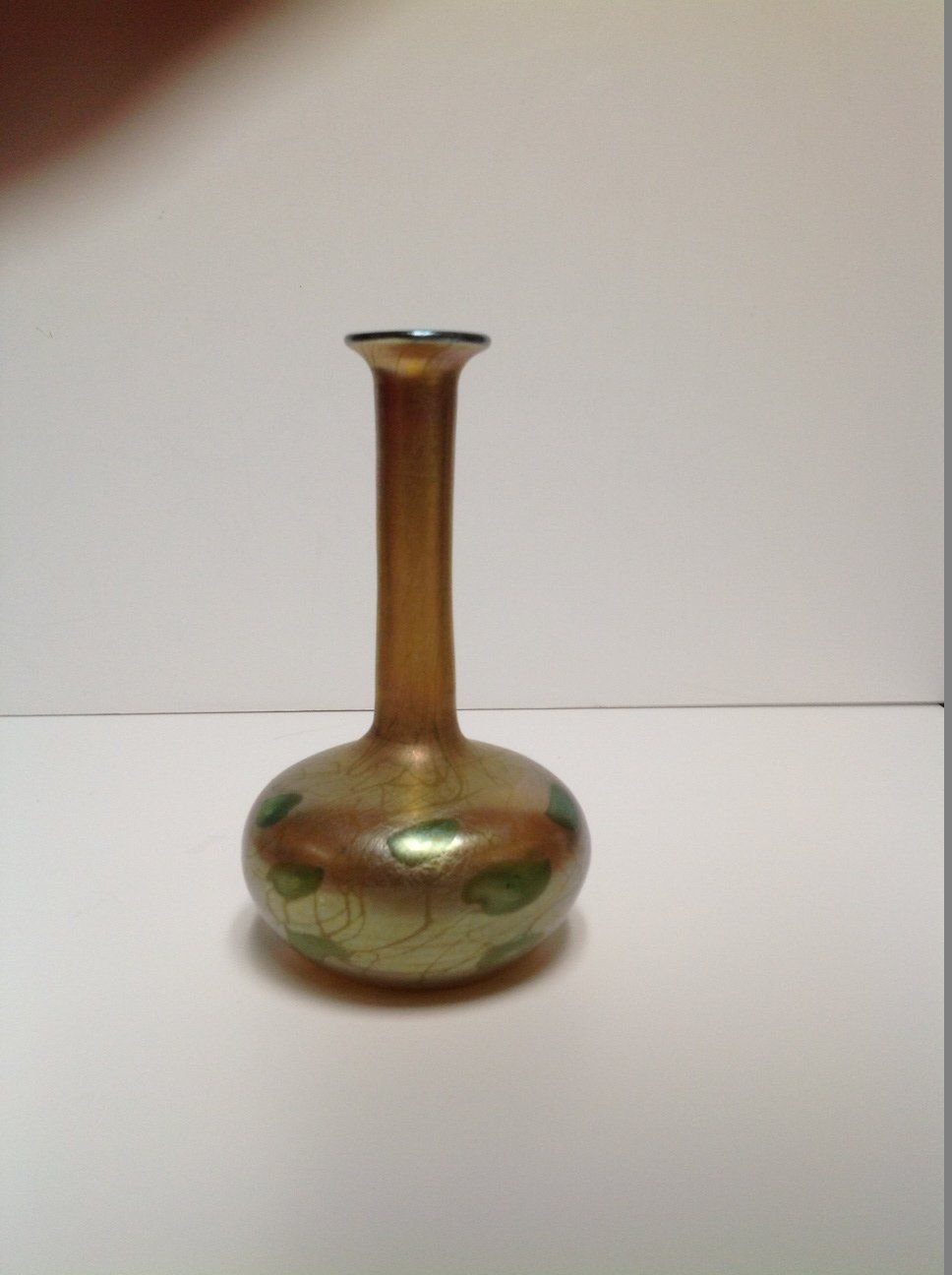 A small vase with a long neck is sitting on a white table.
