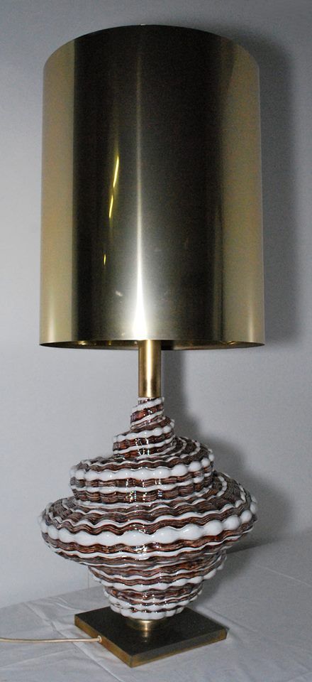Lampada da tavolo con paralume metallico scuro e base decorata con motivi bianchi, marroni e rossi.