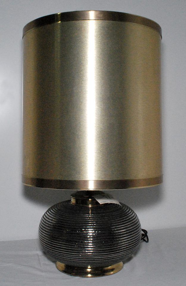 Lampada da tavolo con paralume cilindrico dorato e base sferica nera a coste.