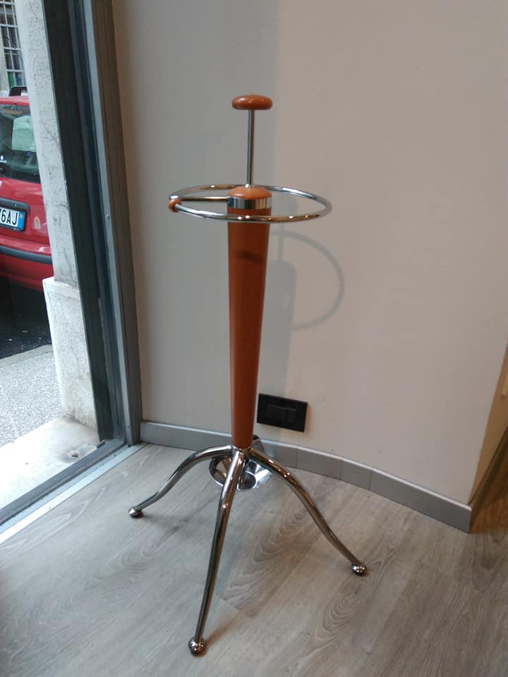 Portabagagli cromato con maniglia arancione posizionato accanto a una porta e a una presa a muro.