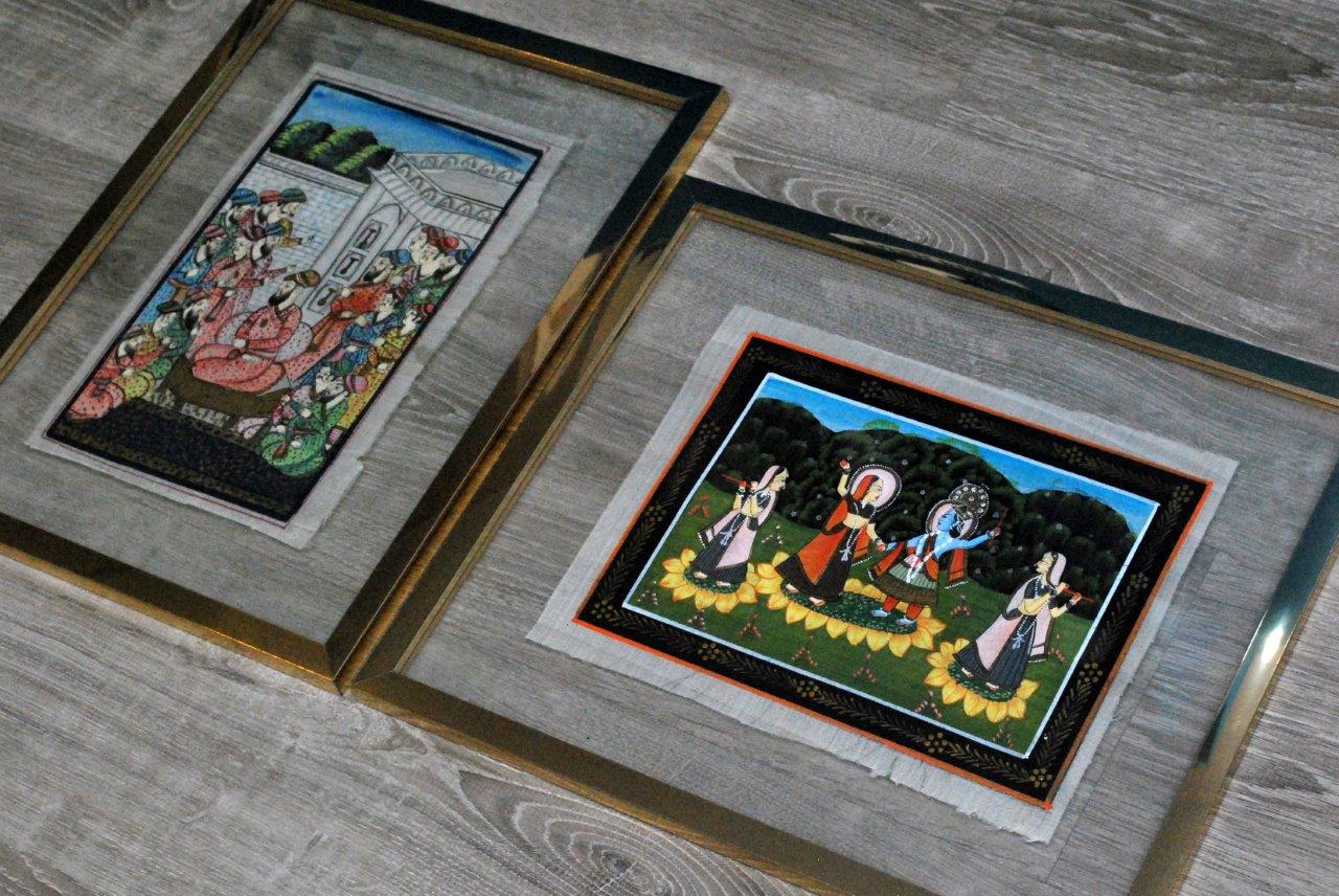 Due opere d'arte colorate incorniciate, appoggiate su una superficie di legno, una in verticale e una in orizzontale.