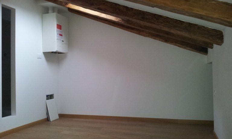 Soffitta vuota con travi di legno inclinate, pareti bianche e un piccolo armadietto a muro.