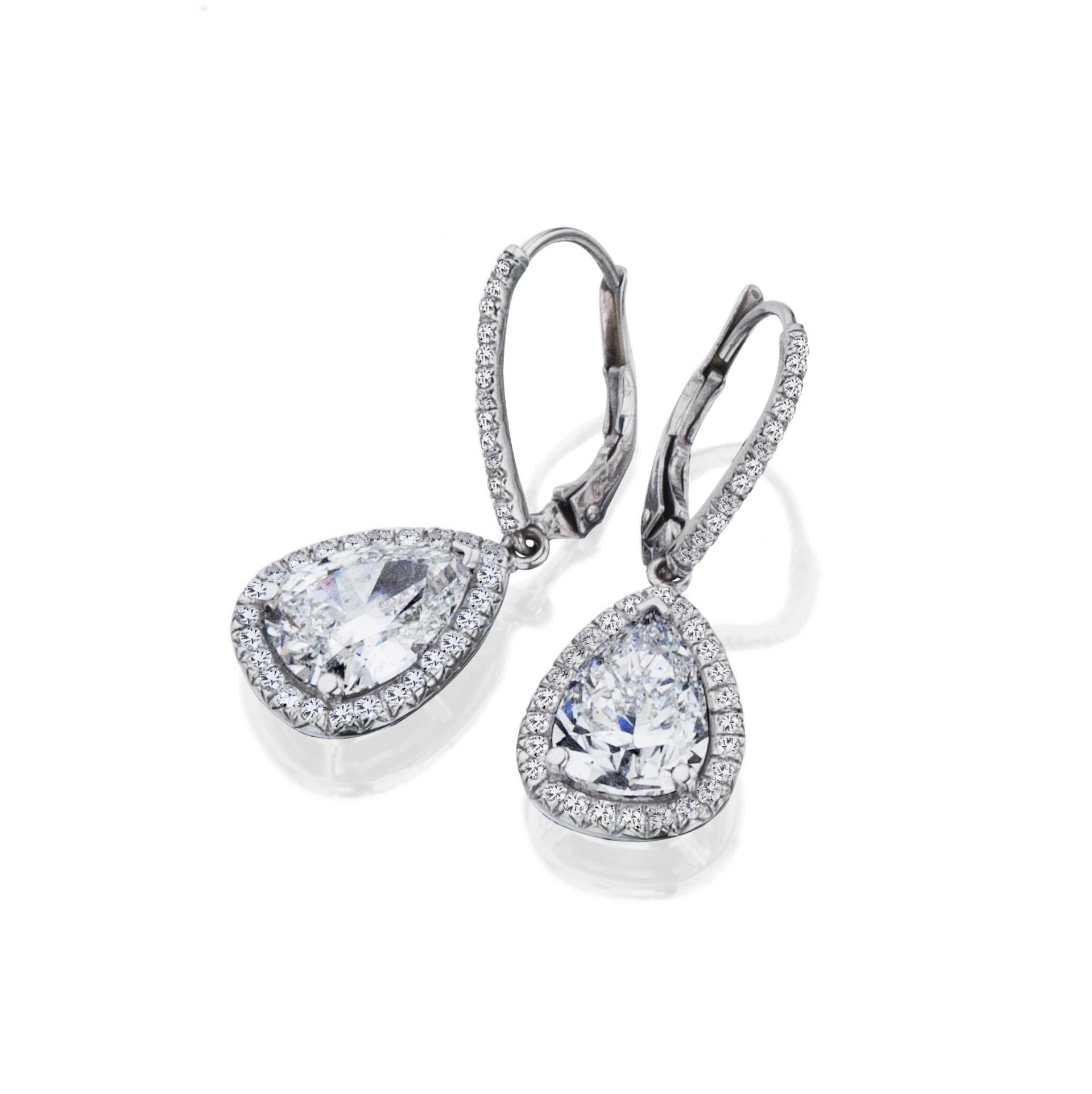 Pair of silver drop earrings with pear-shaped center stones and diamond halos, on a white background.