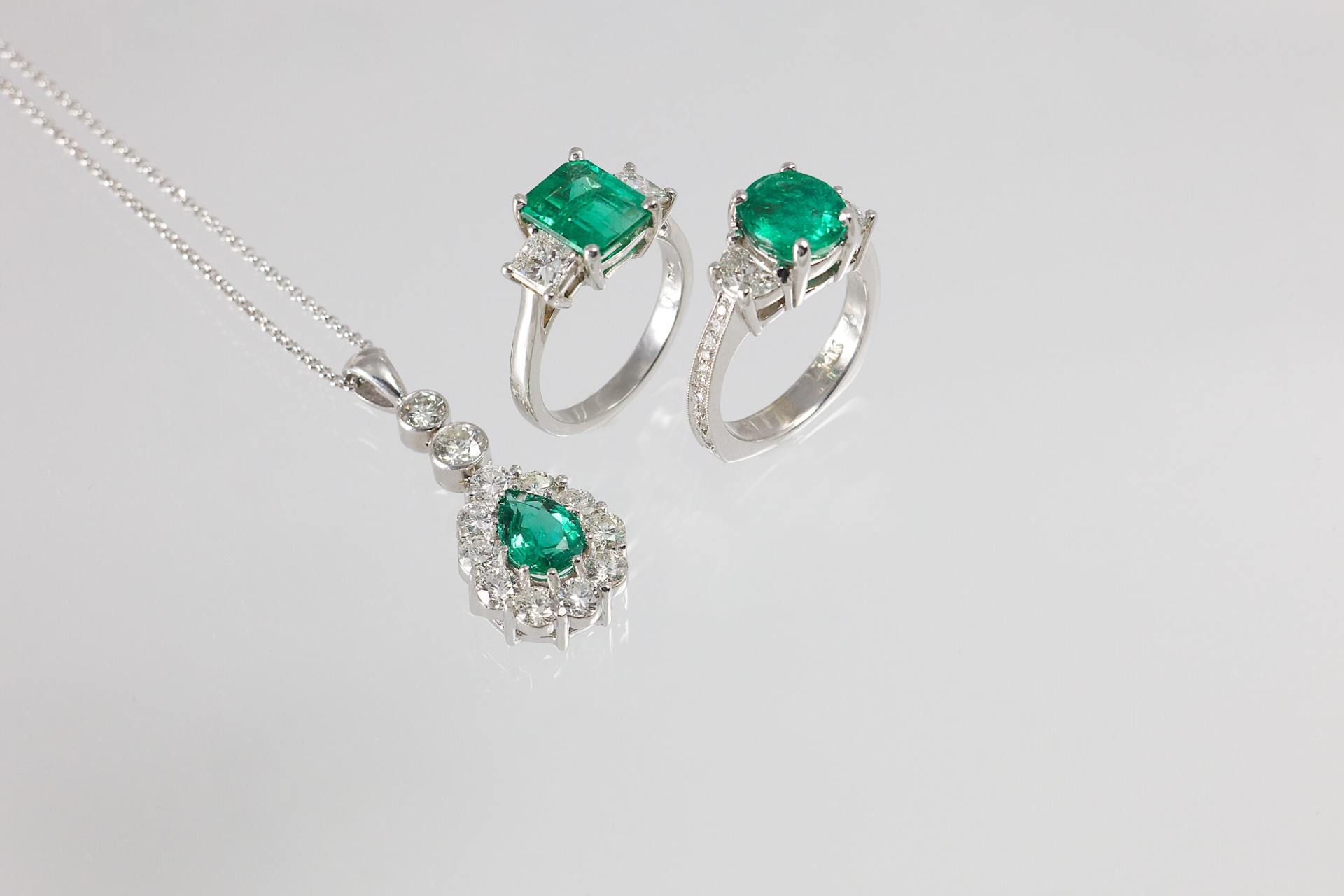 Emerald jewelry set: necklace with pendant and two rings, all with green stones and white metal.