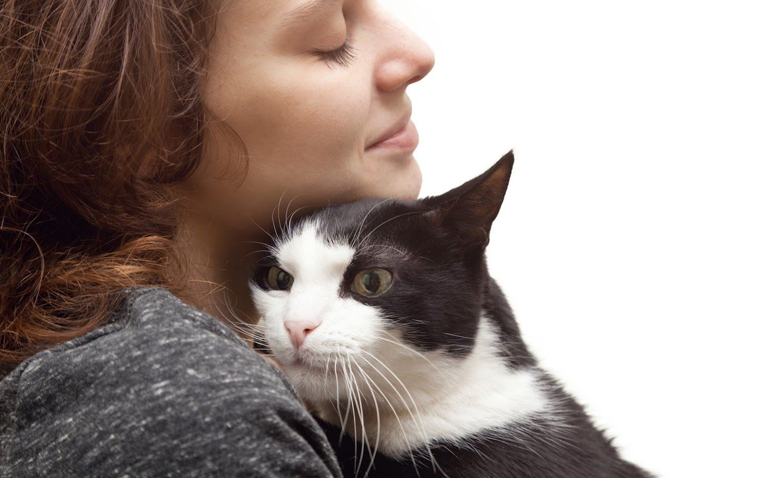 Woman with curly brown hair cuddling a black and white cat, eyes closed.