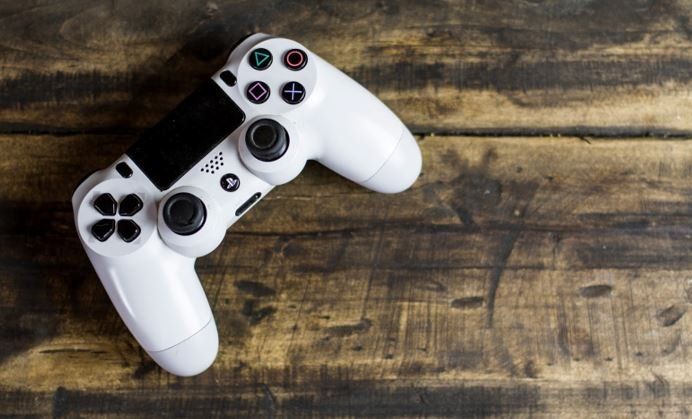 White PlayStation 4 controller on a dark wood surface.