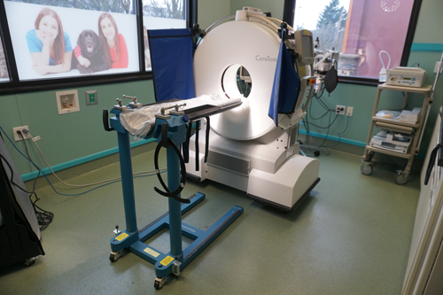 A medical CT scanner with an adjustable table in a brightly lit room.