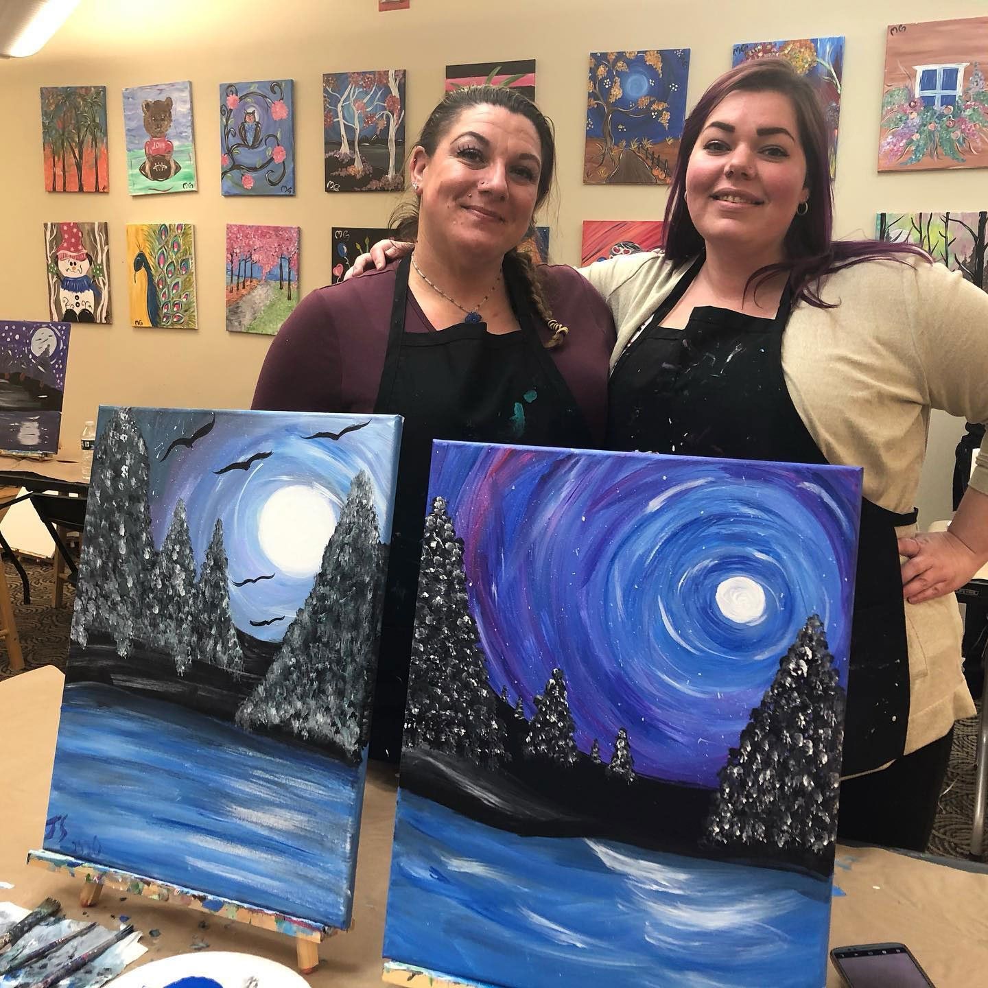 friends posing with their canvases from painting class