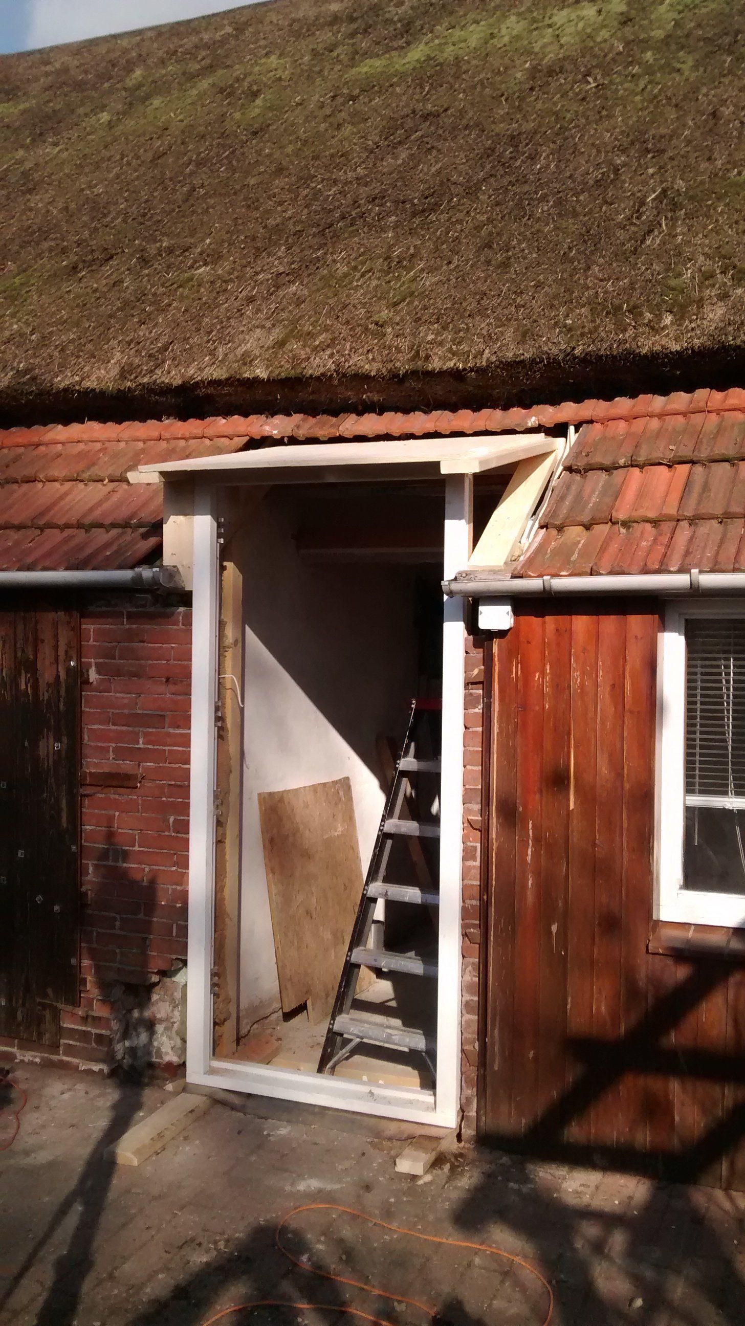 De voordeur van een klein bakstenen huis met een rood pannendak en een trap binnen is open.
