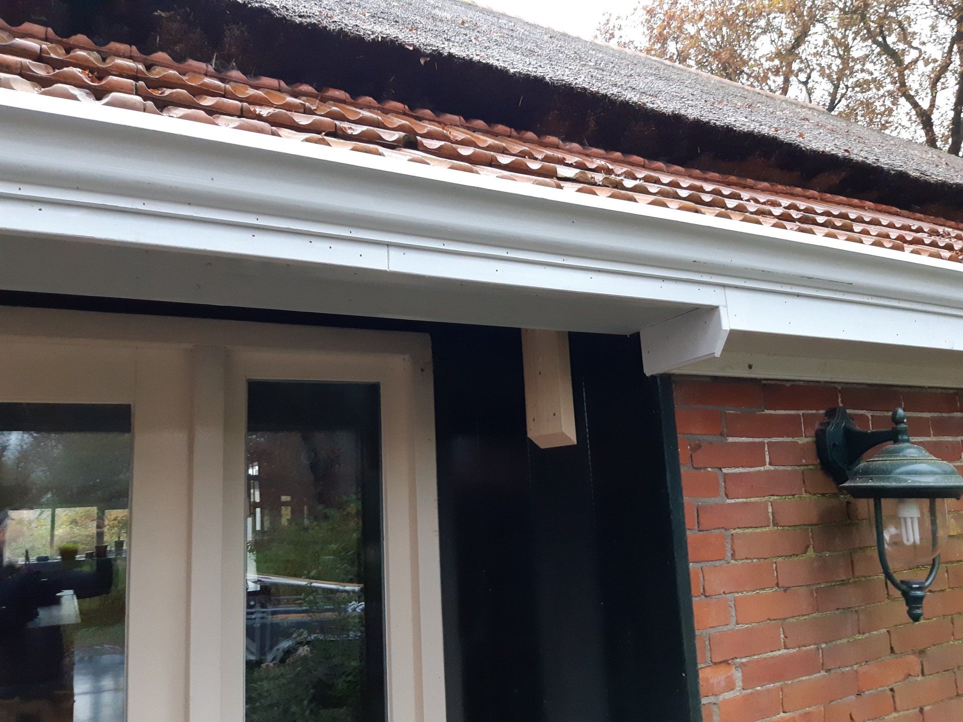 Veranda aan de voorzijde met beige deur, rood pannendak, bakstenen muur en zwarte lantaarnlamp.