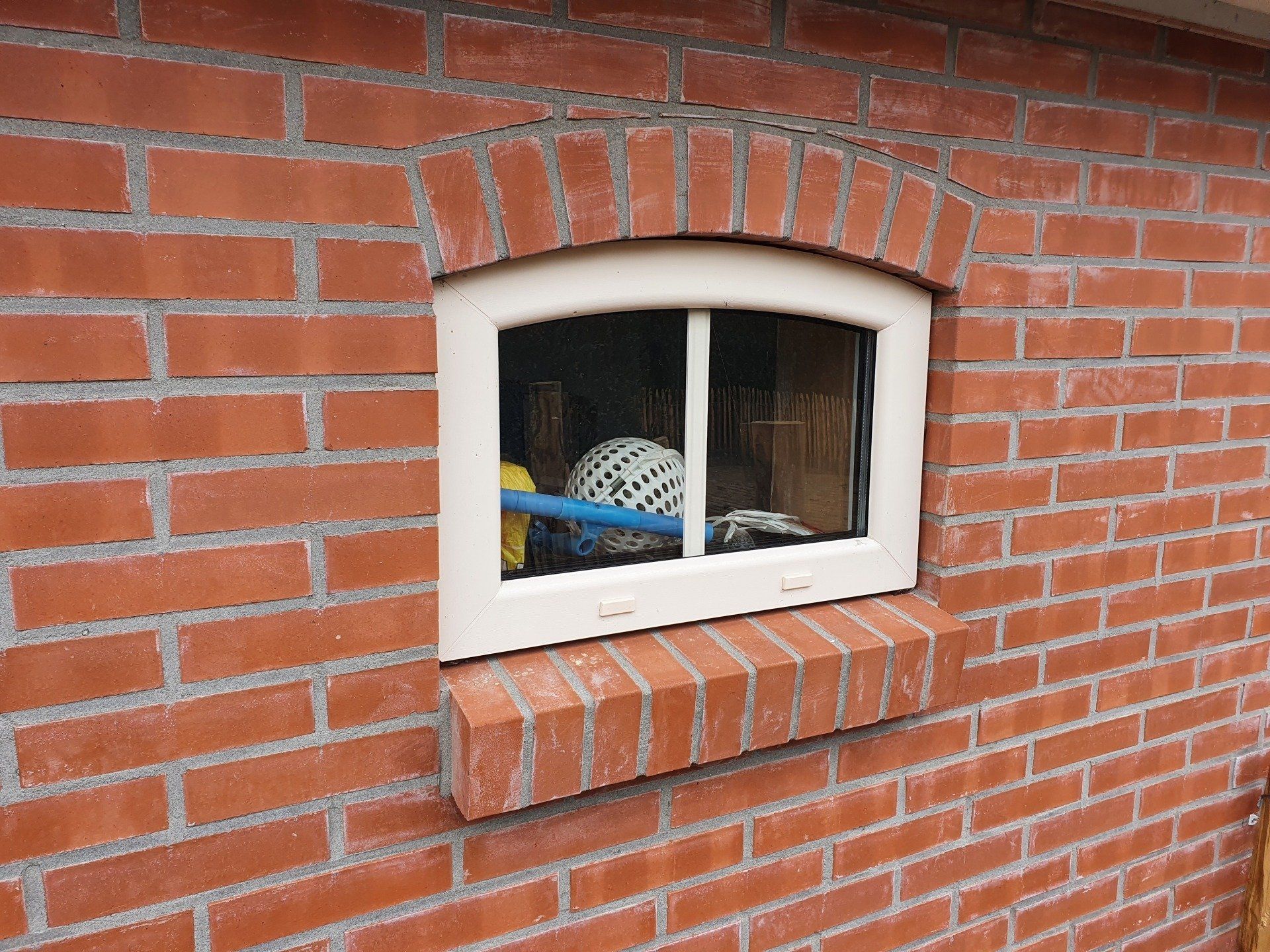 Een klein raam met een wit frame in een rode bakstenen muur, waardoor voorwerpen achter het glas zichtbaar zijn.
