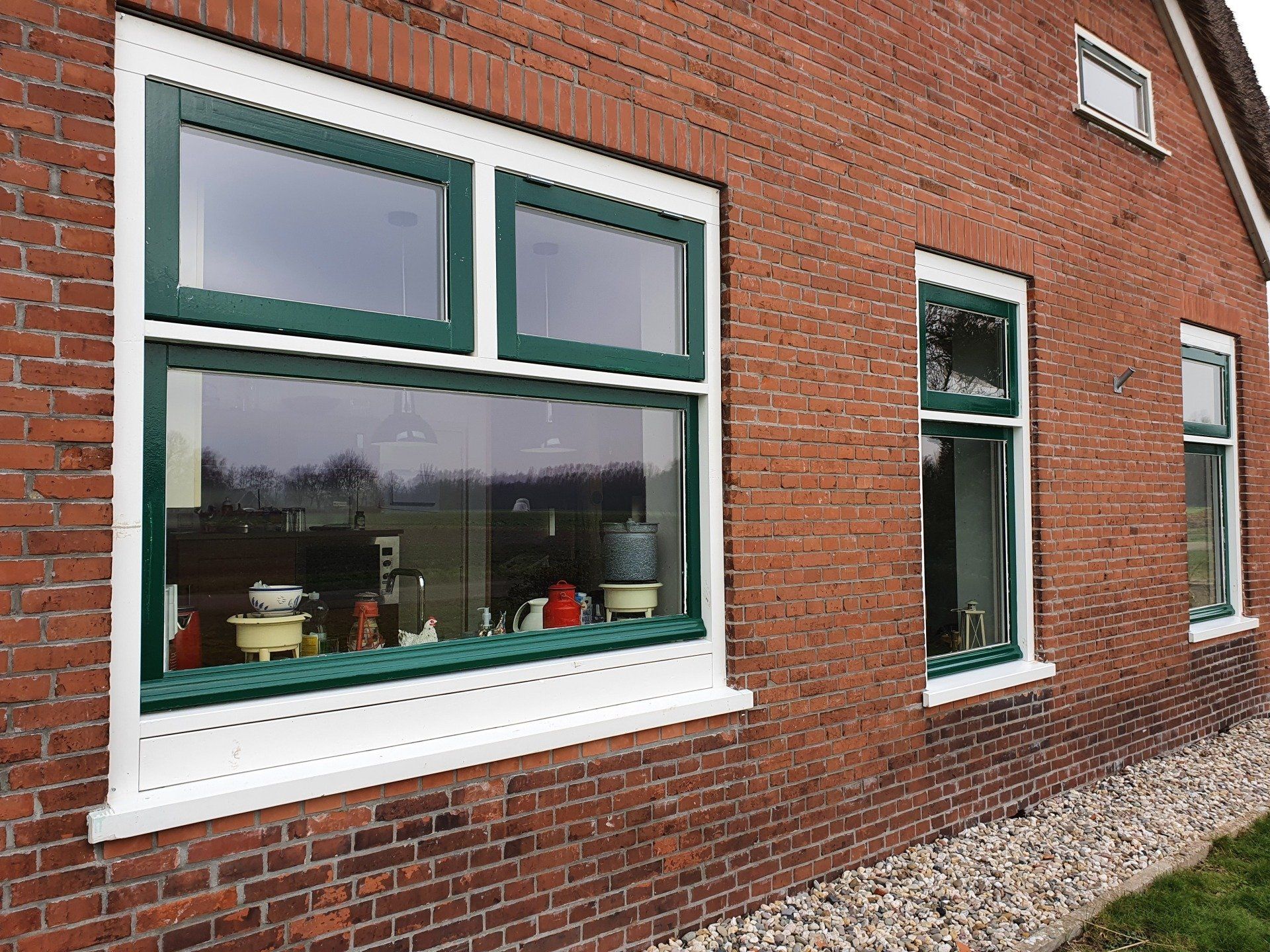 De buitenkant van het huis is opgetrokken uit baksteen, met witte kozijnen rond de ramen en een strook grind langs de muur.