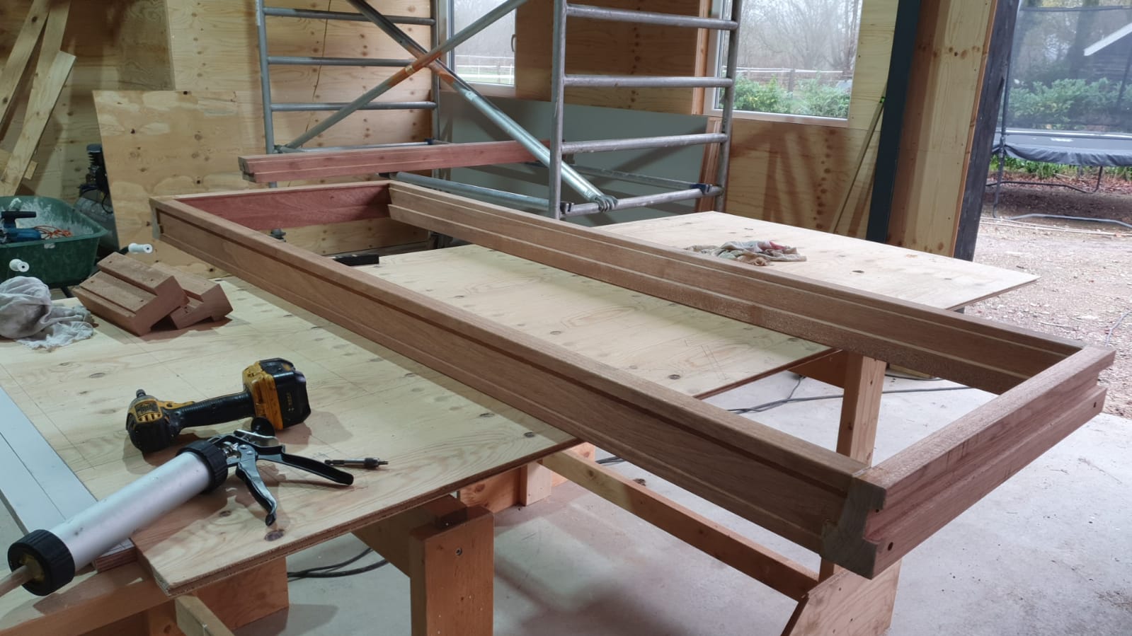Een gedeeltelijk gebouwd houten frame in een werkplaats, met gereedschap en steigers in de buurt.