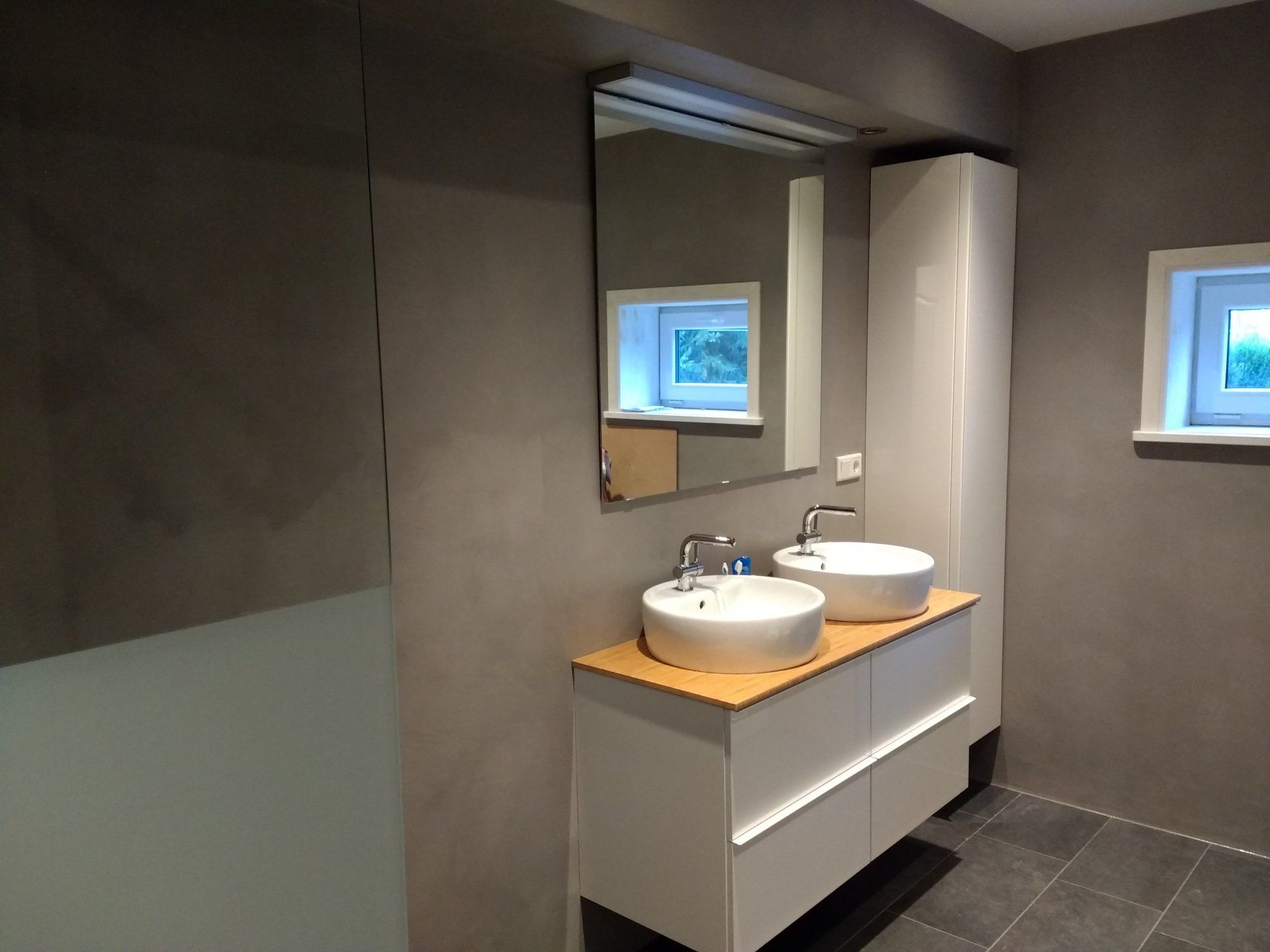 Moderne badkamer met dubbele wastafel, grijze muren, witte kranen en wandspiegels.