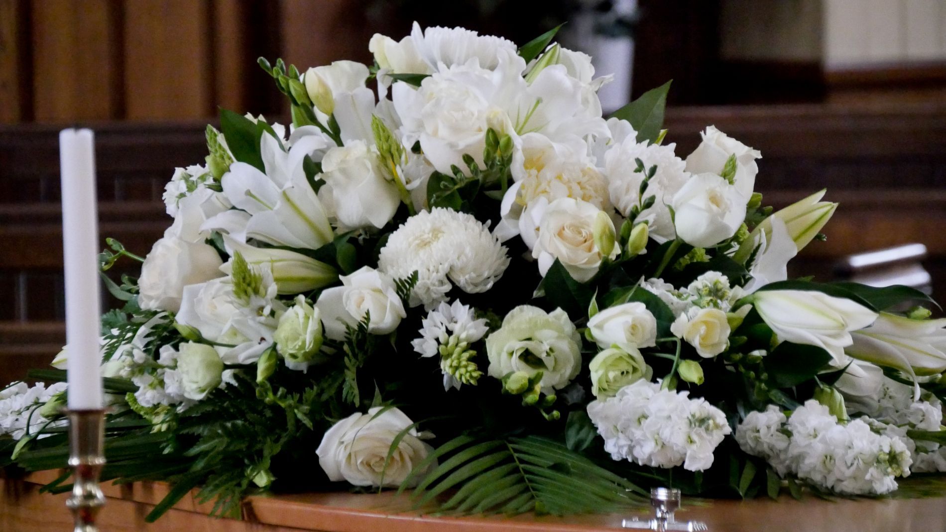 Una bara decorata con fiori bianchi e una candela in una chiesa.