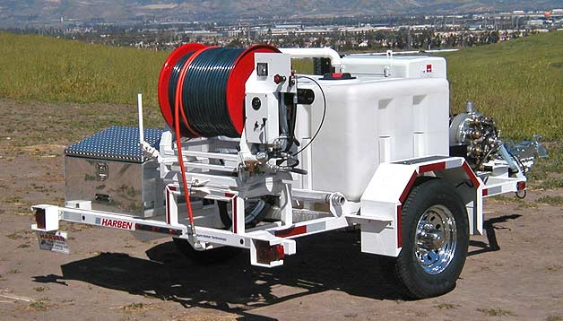 White trailer with red hose reel, water tank, and equipment on a dirt road.