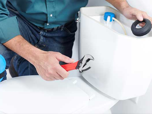 Plumber fixing a toilet; holding wrench and a rubber gasket. White toilet in a bathroom setting.