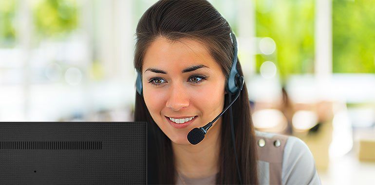 Woman with headset smiling, working on a computer.